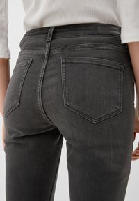 Jeans en denim gris au design ajusté, avec deux poches arrière et une ceinture visible, présentant une texture douce et un léger délavage.