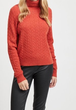 Roter, kabelgestrickter Rollkragenpullover mit geripptem Saum und Bündchen. Kombiniert mit schwarzen Lederhosen. Strukturierter, grober Stoffdesign.