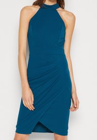 Türkisfarbenes Halfterkleid mit tailliertem Schnitt, Rüschendetails an der Taille und einem diagonalen Wrap-Effekt am Saum, aus weichem Stoff gefertigt.