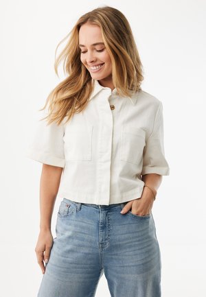 Bílá košile s krátkými rukávy a límečkem, se dvěma náprsními kapsami a jednoduchým zapínáním na knoflík, doplněná světle modrými džínami.