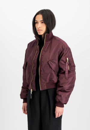 Giacca bomber corta color marrone scuro realizzata in nylon lucido, con una zip dorata, polsini a coste e una tasca con zip sulla manica sinistra.