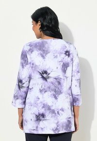 Tunic a maniche lunghe con un motivo floreale viola e bianco, dal taglio rilassato, caratterizzata da un girocollo che valorizza la figura e una texture in tessuto morbido.