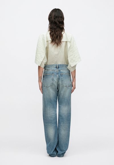 Világoszöld, texturált felső túlnagyított ujjakkal, világoskék, magas derekú, bőszárú farmerrel, mely hátul zsebekkel és kifakult hatással rendelkezik.