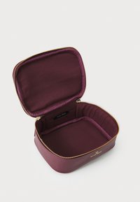 Estuche de cosméticos burdeos hecho de material suave, con un zipper dorado y forro de tela, con forma rectangular y etiqueta de marca en el interior.
