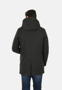 Giacca nera con cappuccio, dal finitura liscia e opaca. Presenta un taglio lungo, tasche laterali e una ventilazione sul retro per migliorare la mobilità.