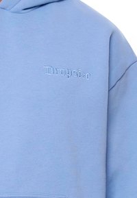 Jasnoniebieska bluza z kapturem wykonana z mieszanki bawełny o miękkiej teksturze. Posiada małe, wyszywane logo "Dropsize" w kontrastowym kolorze.
