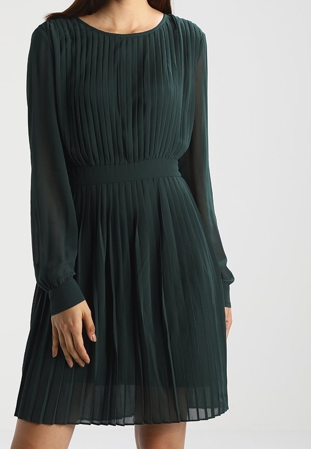Robe vert foncé à manches longues avec des plis verticaux, taille cintrée et jupe évasée, portée par une personne debout des épaules jusqu'à mi-cuisse.