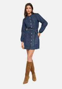 Denimist kleit, millel on istuv vöökoht, pikad puhmvarrukad, nööbitav esikülg ja vööpael; detailidena nööbid ja lühike ääris. Samet-nahast põlviksaapad.