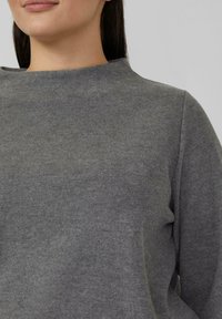 Grauer Strickpullover mit hohem Kragen und langen Ärmeln, der eine weiche Textur und ein schlichtes, lässiges Design aufweist.