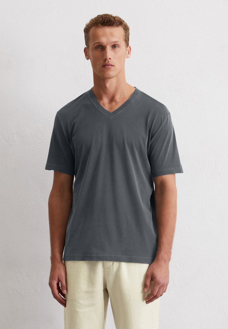 T-shirt gris à manches courtes et col en V, en mélange de coton, texture lisse, coupe décontractée, associé à un pantalon de couleur claire. Design simple sans ornements.