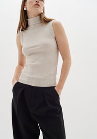Vaalean beige ilmanhihaisen korkeakauluksisen paidan, jossa on ribbikuvio, yhdistettynä korkeavyötäröisiin mustiin housuihin, jotka antavat rennon ilmeen.
