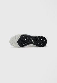 Black textured outsole with white accents, featuring a patterned tread design and logo. Smooth white midsole integrates with a flexible shape.