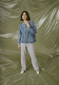Denim jacket with pearl accents, featuring a quilted pattern and button front, paired with gray sweatpants and white pointed shoes.