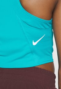 Top sportivo turchese realizzato in materiale testurizzato. Presenta un collo rotondo e il logo Nike bianco sul lato, abbinato a pantaloni corti color marrone scuro.