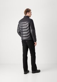 Black puffer jacket with a high collar and quilted design, featuring a smooth texture. Paired with black jeans and sturdy black shoes.