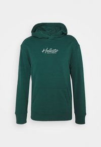 Mörkgrön munkjacka med huva, framficka och vitt "Hollister California"-logotyp på bröstet, visas mot en vit bakgrund.