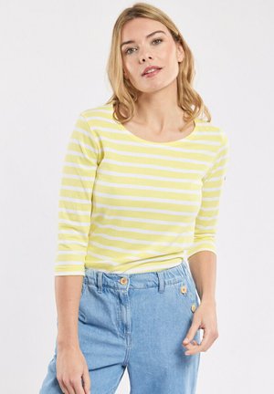 Chemise à rayures jaunes et blanches à manches longues avec un décolleté large, associée à un pantalon en denim bleu clair taille haute avec des boutons à l'avant.