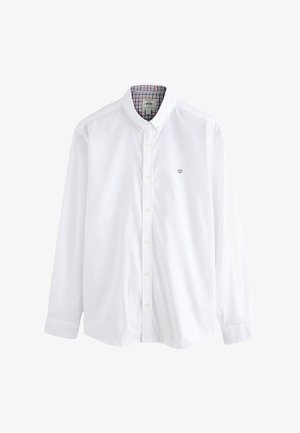 Chemise blanche boutonnée avec un col structuré, présentant un motif à carreaux contrastant à l'intérieur du col et un petit emblème brodé sur la poitrine.