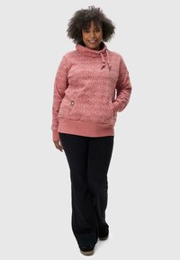 Fleece hoodie in rose with textured pattern, cowl neck, drawstring, and kangaroo pocket. Paired with black flared pants and dark shoes.