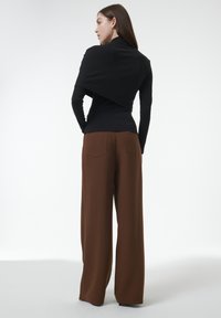 Schwarzes Langarmoberteil kombiniert mit braunen weiten Hosen, die über eine rückwärtige Naht und seitliche Taschen verfügen, mit einer glatten, weichen Textur.