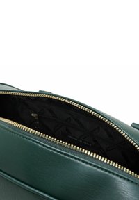 Borsa in pelle verde scuro con cerniera dorata parzialmente aperta, che rivela un interno in tessuto nero con tasca con cerniera e logo Armani Exchange.