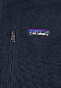 Mørkeblå strikfleecejakke med frontlynlås og et sort Patagonia-logo patch med en flerfarvet bjergsilhuet.