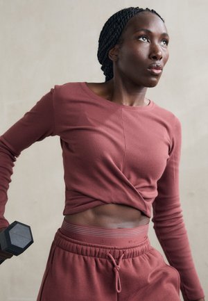 Maroon athletic set with a long-sleeve top and high-waisted pants. The top features a twisted design, and the pants have a logo waistband.