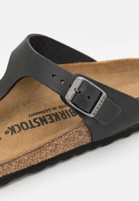 Black sandal with a smooth leather strap, silver metal buckle, and cork footbed. Features a textured, dark rubber sole for grip.