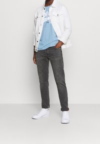 Bílá džínová bunda, světle modré tričko s potiskem, tmavě šedé džíny, bílé tenisky. Ležérní outfit s viditelným šitím a detaily s ohrnutými lemy.