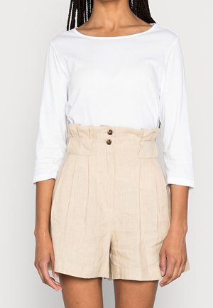Femme portant un short beige taille haute avec une taille paperbag et des détails à boutons, assorti à un haut blanc à manches trois-quarts.