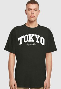 Čierne bavlnené tričko s výrazným bielym textom "TOKYO" v oblúkovom dizajne, s doplnkovým textom nižšie. Krátke rukávy a okrúhly výstrih.
