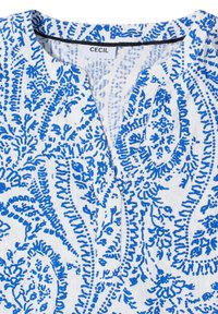 Haut en tissu blanc avec des motifs floraux et cachemire bleus complexes, doté d'un col en V arrondi et d'une étiquette de marque « Cecil » au col.