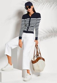Navy en wit gestreepte ribbel lange mouwen cardigan, witte cropped broek, witte sneakers en een beige handtas met bruine accenten.