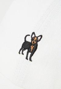 Perro pequeño bordado en negro y marrón sobre tela blanca, mostrando un detallado bordado y textura.