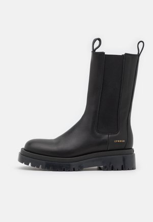 Botte noire en cuir mi-mollet avec semelle crantée épaisse, panneau latéral élastique, languettes de traction et petit marquage doré "CPNHGN" près du talon.