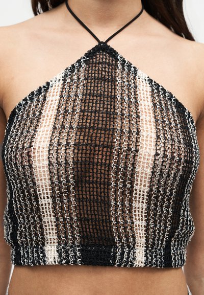 Haut à bretelles en maille à carreaux noirs et blancs porté par une personne, montrant la peau visible à travers le tissu semi-transparent.