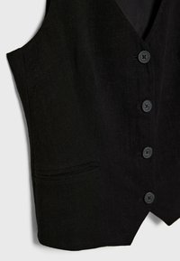Gilet noir sur mesure avec quatre boutons et deux poches passepoilées sur fond uni.