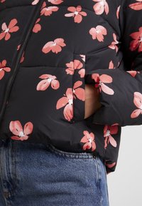 Svart puffjacka med rosa blommönster, dragkedjestängning och sidofickor. Strukturerad tyg med en slät finish. Bärs över denimjeans.