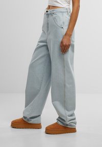 Jeans de tiro alto en denim de color azul claro, con costuras en contraste y bolsillos laterales, combinados con zapatos de ante marrón claro tipo slip-on.