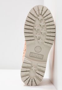 Tige de chaussure orange perforée avec une semelle en caoutchouc beige. La semelle présente des rainures et un logo Timberland au centre.