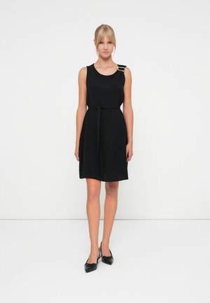 Black sleeveless dress with a tie waist, featuring a curved neckline and a decorative buckle on one shoulder. Smooth fabric texture.