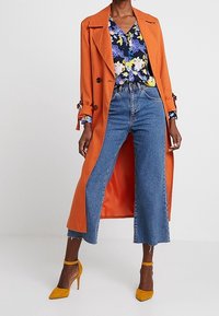Oranžový trenčkot s květinovou blůzou, vysokými denimovými culotty a žlutými lodičkami. Má uvolněný střih a kontrastní vnitřek.