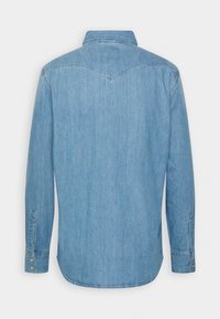 Chemise en denim bleu clair à manches longues avec poignets boutonnés et un détail en forme de pointe sur le dos.