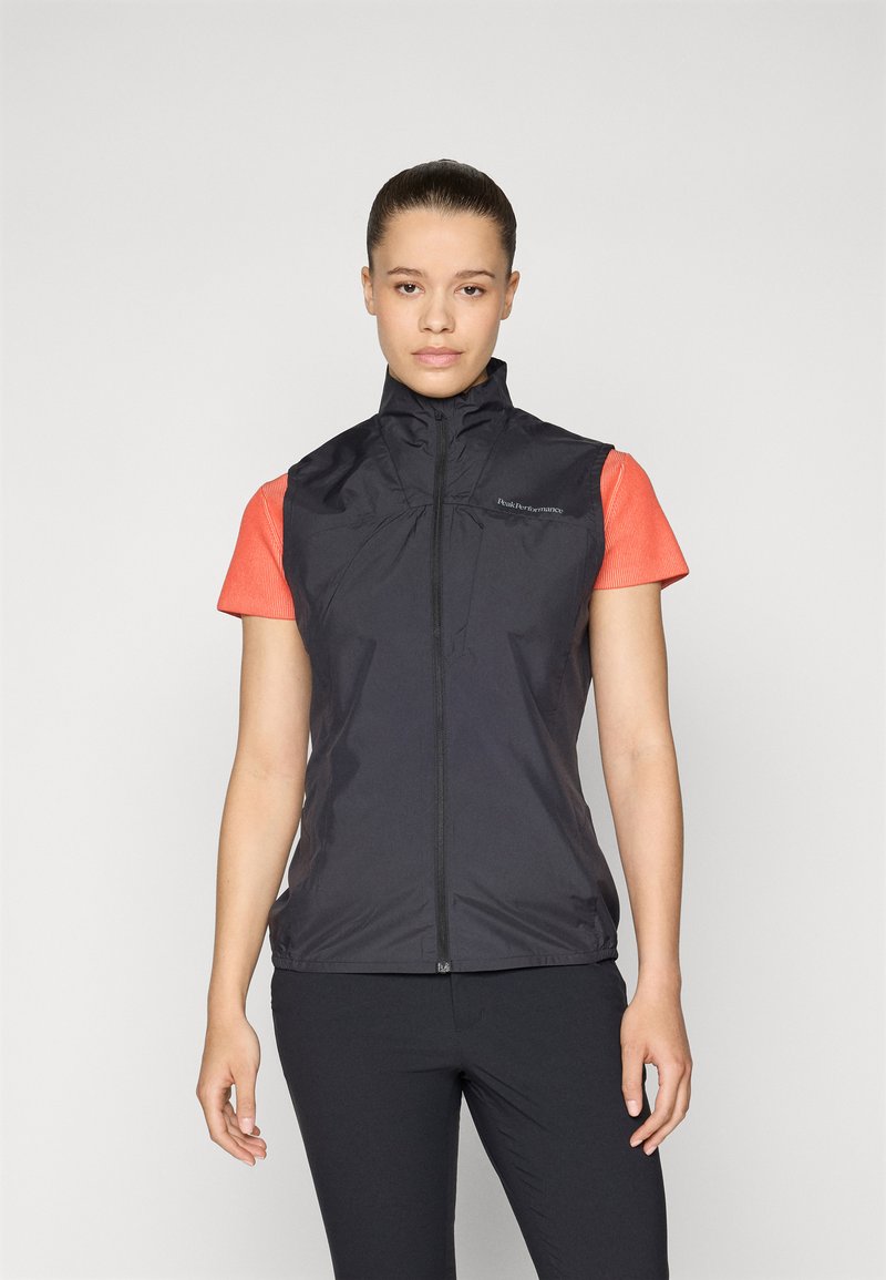 Black lightweight vest with high collar and front zipper, worn over a bright orange short-sleeve shirt. Smooth texture and minimal branding.