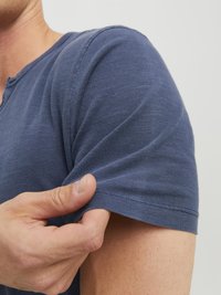 T-shirt z krótkim rękawem w kolorze granatowym, wykonany z miękkiego materiału, z prążkowanym dekoltem i luźnym krojem, z widocznymi detalami ściegów w okolicach rękawów.