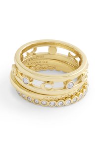 Guldtonade stapelringar med olika mönster, inklusive släta band, en med en "C"-accent och en annan prydnad med klara rhinestones.