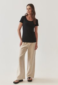 T-shirt noir à manches courtes avec un col dégagé associé à un pantalon large en lin beige clair et des sandales glissantes noires.