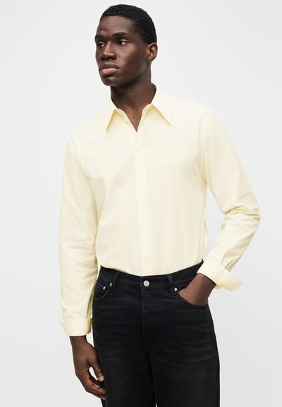 Jasnożółta koszula z długim rękawem wykonana z bawełny, z kołnierzykiem w szpic i zapinana na guziki, zestawiona z ciemnymi jeansami.