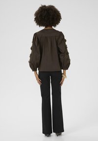 Brown, long-sleeve blouse with puffed sleeves and floral accents. Paired with black, flared trousers. Smooth fabric, classic design.