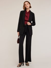 Zwarte op maat gemaakte pak met een dubbelzijdig colbert, gecombineerd met een bordeaux blouse, wijde broek en zwarte gestructureerde hakken. Een kleine handtas is inbegrepen.